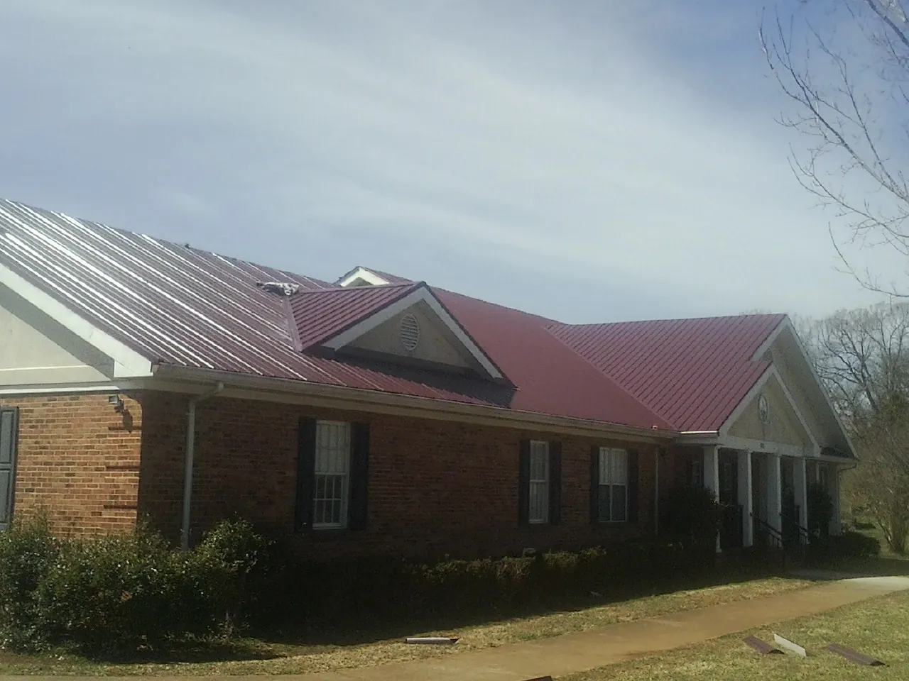 Red metal roof with gabled entries on a long brick building, from a Hail Damage Roof Repair job in Laguna Niguel