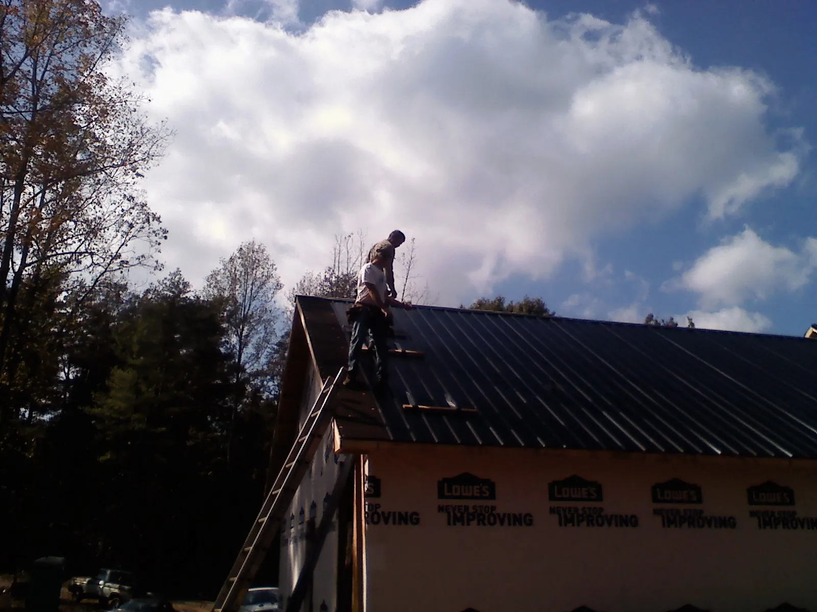 Roofer fastening dark metal panels high against a cloudy sky, from a Roof Inspection job in Laguna Niguel