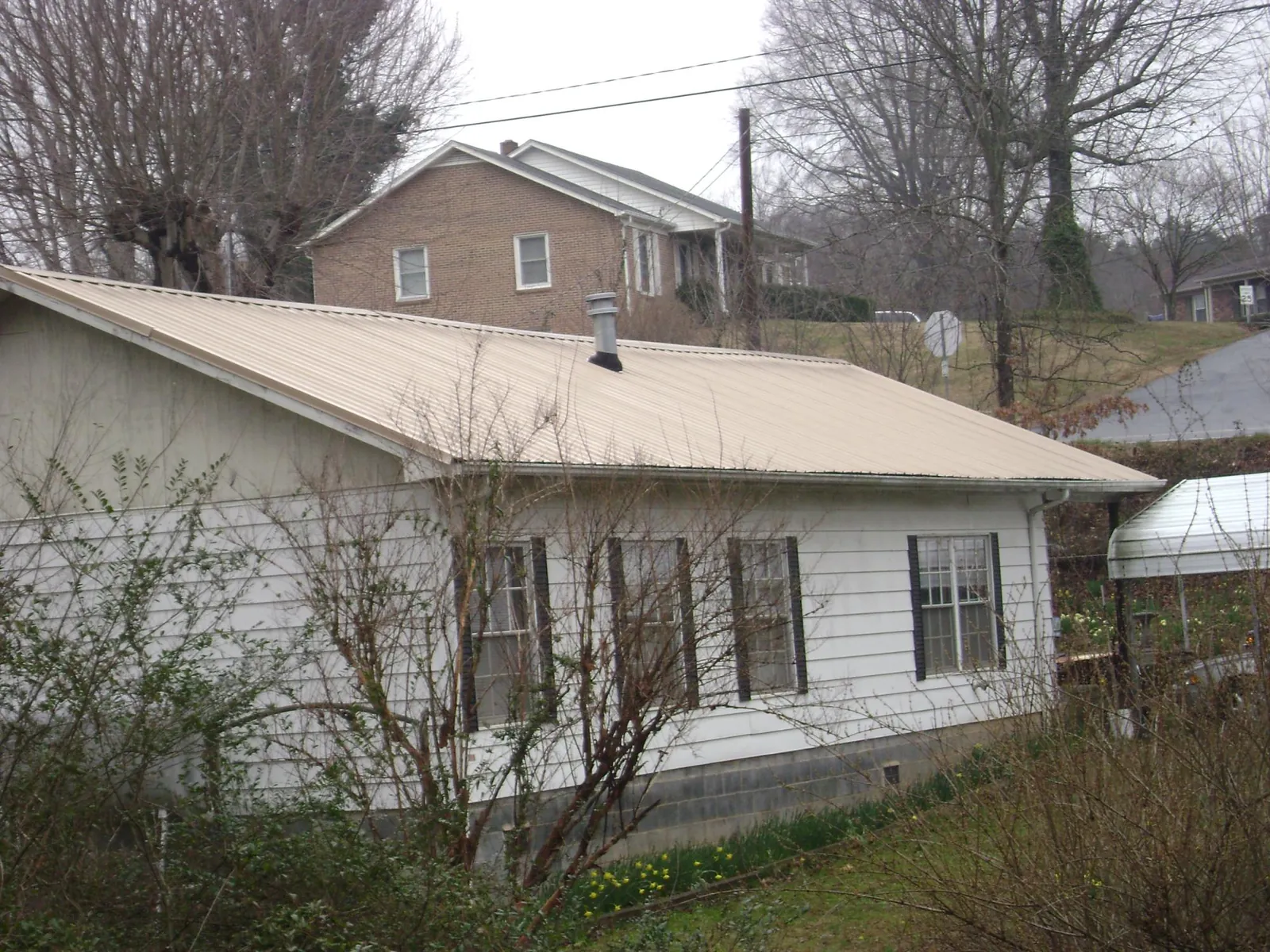 Tan metal roof on a white sided house set into a hillside — Commercial Roofing by Roofing Brothers in Laguna Niguel